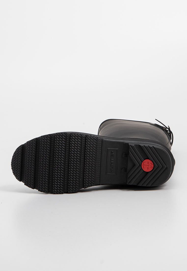 Schwarzer Gummistiefel mit einer strukturierten schwarzen Sohle, versehen mit einem roten kreisförmigen Akzent an der Ferse und einem abgerundeten Toe-Design.