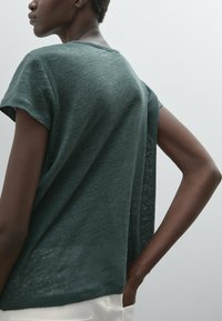 Donkergroene korte mouwen top met een losse pasvorm, voorzien van een ronde halslijn en een textuur, lichtgewicht stof. Tovendoor stitching detail langs de naden.