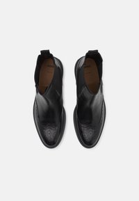 Bottines en cuir noir avec panneaux latéraux élastiques, ornées de détails brogue et d'une finition lisse. Semelle en caoutchouc pour adhérence et confort.