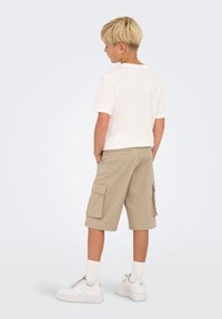 T-shirt blanche à manches courtes, shorts cargo beiges avec poches latérales, baskets blanches à semelles texturées et chaussettes blanches côtelées.