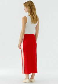 Jupe maxi en tricot rouge avec des rayures blanches sur les côtés, associée à un débardeur blanc ajusté ; texture lisse et longueur jusqu'aux chevilles.