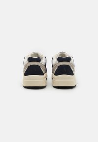 Marineblå og kremfargede joggesko med overdel i semsket skinn og mesh, strukturert design og kontrasterende beige aksenter på hælen og sidene.