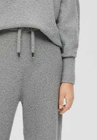 Grijs fleece lounge set met een gestructureerde, zachte afwerking. De top is losvallend met een trekkoord; de broek is relaxed met elastische boorden.