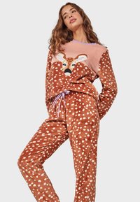Fleece pajama set in brown with white polka dots, featuring a pink top with a deer graphic. Soft texture and drawstring waist.