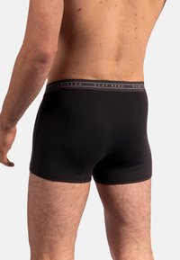 Svarta boxershorts i glatt tyg, med ett brett elastiskt midjeband med texten "OLAF BENZ" i grått. Enkel, figurnära design.