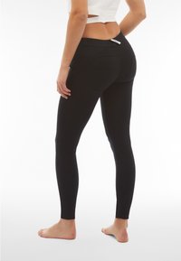 Mustat legginssit, joissa on sileä pinta, keskikorkea vyötärö ja erottuva sauma takataskuissa. Istuu tiiviisti jalkoihin.