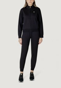 Completo sportivo nero composto da giacca con zip e colletto alto e pantaloni coordinati. Realizzato in tessuto liscio, con polsini a coste e dettagli con logo.