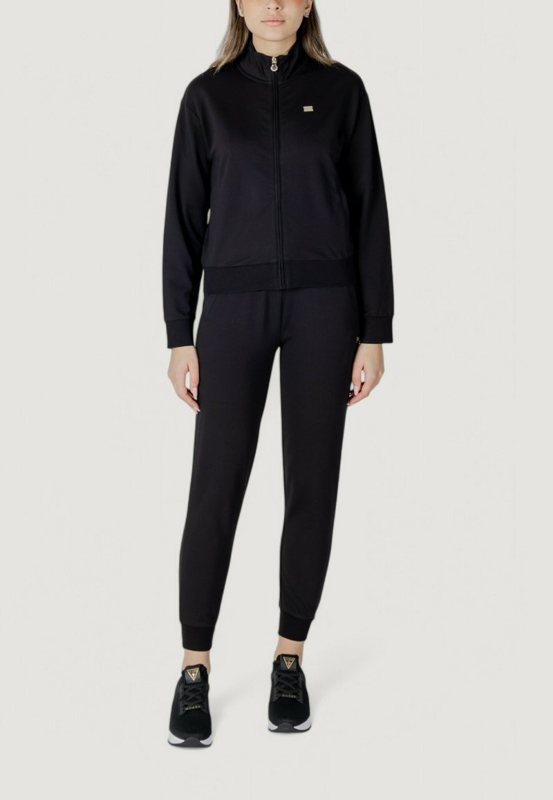Completo sportivo nero composto da giacca con zip e colletto alto e pantaloni coordinati. Realizzato in tessuto liscio, con polsini a coste e dettagli con logo.