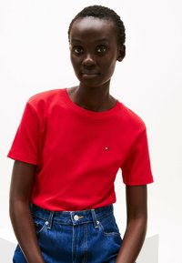 Rode katoenen T-shirt met een ronde hals en korte mouwen, met een klein logo op de borst. Gepaard met hoge blauwe denim jeans.