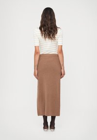 Brun strikket maxiskjørt med ribbestrikket midjebånd, kombinert med en tettsittende hvit stripet topp. Glatt tekstur, hel-lengde design.