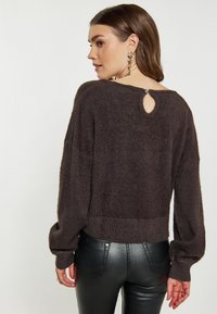 Ciemnobrązowy, puszysty sweter o luźnym kroju, z prążkowanym dołem i wycięciem na plecach, zestawiony z dopasowanymi czarnymi legginsami.