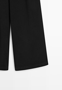 Pantaloni neri a gamba larga realizzati in tessuto morbido, con una texture liscia e orli puliti, silhouette dritta e senza chiusure visibili.