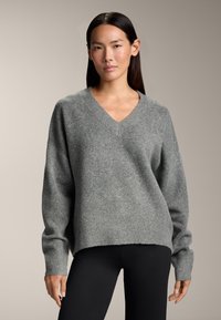 Szürke, V nyakú pulcsi, puha kötött anyagból készült. Esésben lévő vállvarrásokkal és bordás mandzsettákkal rendelkezik, laza szabású. Fekete leggings-szel viselik.
