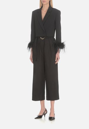 Blazer nero cropped con dettagli di piume sulle maniche, abbinato a pantaloni neri a gamba larga e décolleté slingback neri a punta.