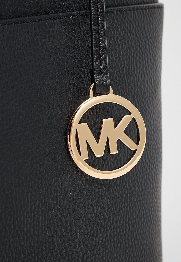 Zwarte gestructureerde leren oppervlakte met een hangende gouden cirkelvormige hanger met de initialen "MK" in het midden.