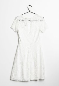 Robe en dentelle blanche à manches courtes, avec un motif floral, un dos en trou de serrure et une jupe évasée, suspendue à un crochet noir.