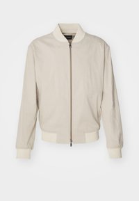 Veste bomber beige clair avec zip à l'avant, poignets et ourlet côtelés, et une texture de tissu douce. Présente un design minimaliste sans motifs.
