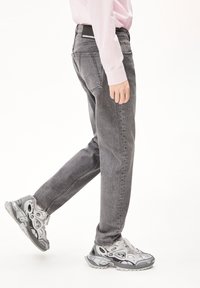 Graue Denim-Jeans mit geradem Schnitt und Five-Pocket-Design, kombiniert mit klobigen grauen Sneakers mit Cut-Out-Akzenten und Gummisohlen.