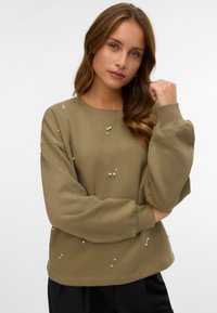 Olijfgroene sweatshirts met verlaagde schouders en parelversieringen. Beschikt over een ronde hals en ribgebreide manchetten. Zacht, katoenmix stof.