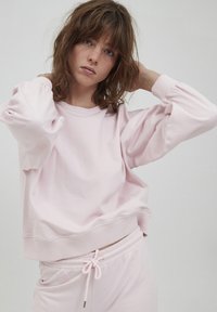 Felpa rosa realizzata in tessuto morbido, con vestibilità rilassata, polsini a coste e scollatura ampia, abbinata a pantaloni jogger coordinati.