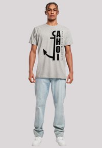 Graues Baumwoll-T-Shirt mit einem großen schwarzen Anker-Design. Der Text "AHOI KNUT & JAN HAMBURG" ist in vertikaler Ausrichtung neben dem Anker gedruckt.