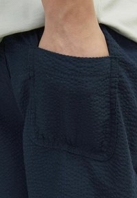 Tissu texturé bleu marine avec un détail de poche visible. Le matériau semble légèrement matelassé, avec un motif doux et en relief et des bords finis.