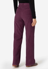 Weite Beinhosen in einem tiefen Pflaumenton, gefertigt aus strukturiertem Stoff. Mit Gesäßtaschen und einem hohen Taillendesign. Sauberer, gerader Schnitt mit minimalen Akzenten.