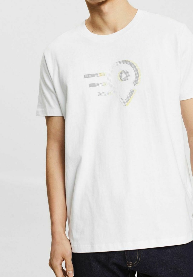 T-shirt en coton blanc avec un motif graphique en gris et jaune, parsemé de motifs en pointillés. Manches courtes et coupe décontractée.