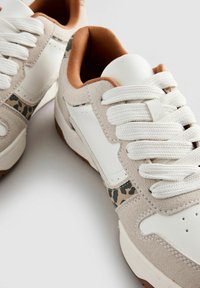 Valged ja beežid sneakers, mis on valmistatud sametist ja nahast, leopardimustriga aksendiga, valgete paeltega ja pruuni sisemusega.