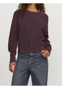 Pullover di lana color viola scuro con un design a coste testurizzato, scollatura rotonda e maniche lunghe, abbinato a jeans in denim a vita alta.