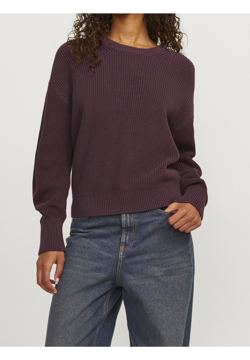 Pullover di lana color viola scuro con un design a coste testurizzato, scollatura rotonda e maniche lunghe, abbinato a jeans in denim a vita alta.