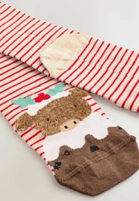 Calcetines a rayas en rojo y crema, con un diseño texturizado de un oso marrón en un pie y detalles navideños en la tela.