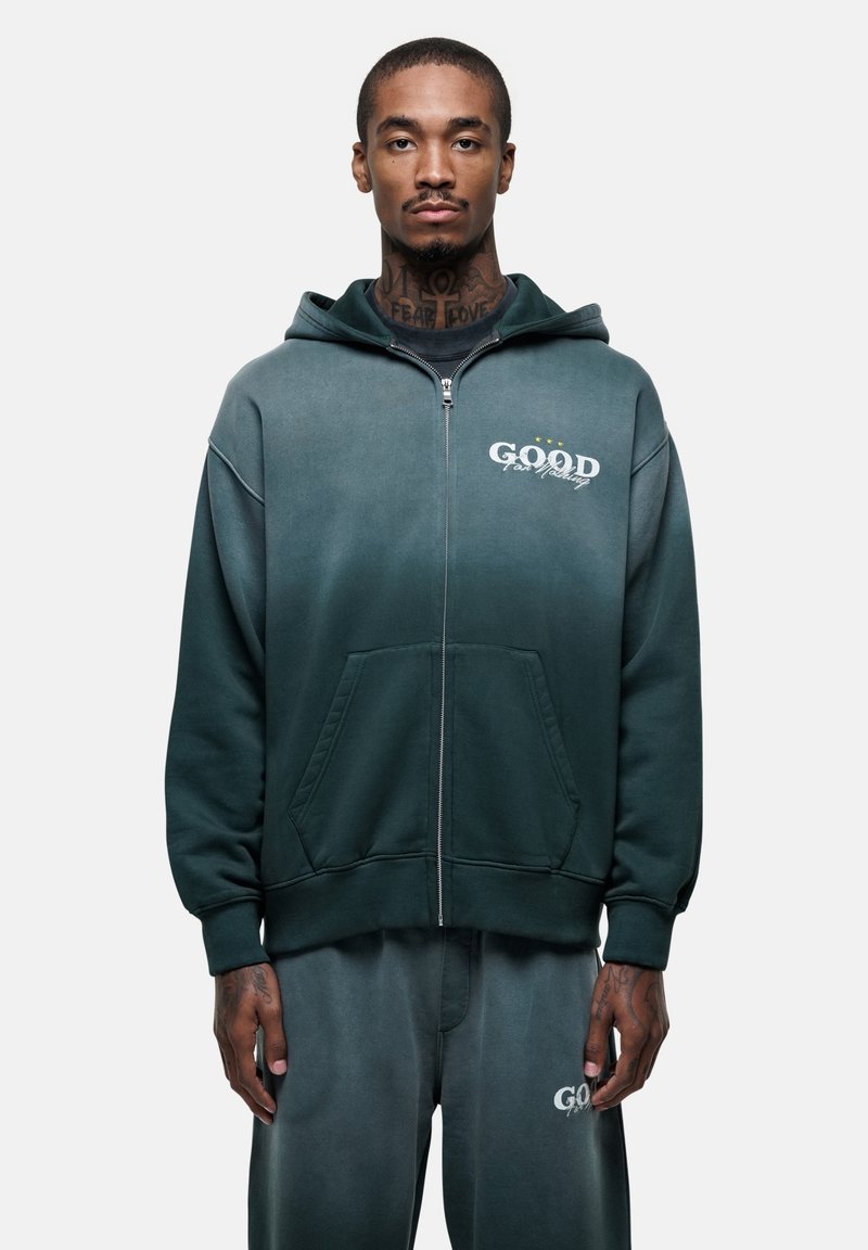 Felpa con cappuccio e zip in tessuto verde sfumato. Presenta tasche frontali, polsini a coste e il logo "GOOD" con dettagli bianchi.