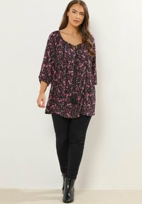 Tunic nera a motivo paisley con maniche a tre quarti e scollatura a V. Presenta un accento con nappina all'neckline. Abbinata a pantaloni skinny neri e stivali.