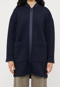 Námořnická modrá oversized mikina s kapucí na zip, která má dvě velké kapsy a měkkou, texturovanou látku. Design s kapucí a širokými rukávy.