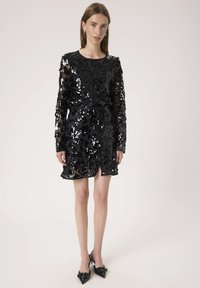 Rochie neagră cu paiete, cu mâneci lungi, decolteu rotund și un cordon la talie. Prezintă o deschidere până la coapsă și un model texturat.