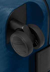 Primo piano di ruote nere a doppio spinner attaccate all'angolo di una valigia textured di un blu scuro.