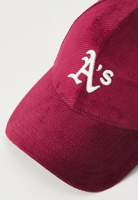 Burgundijas krāsas korduroja cepure ar baltu izšūtu "A's" logotipu priekšpusē, strukturētā formā un ar teksturētu apdari.