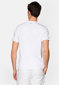 Biała koszulka z krótkim rękawem wykonana z bawełny, z okrągłym dekoltem i małym nadrukowanym logo na górnej części pleców. Gładka tekstura.