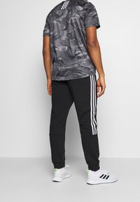Grijs camouflage t-shirt met korte mouwen voor atleten, met drie witte strepen op de rug, gecombineerd met zwarte getailleerde joggers met witte zijkanten.