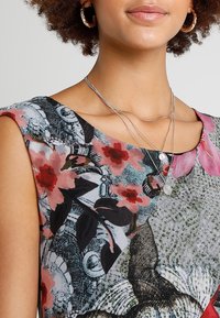 Hihaton paita, jossa on kukkakuvio ja sekoitus vaaleanpunaisia ja mustia sävyjä. Hopeiset kerrokselliset kaulakorut ja renkaankorvakorut täydentävät asua.