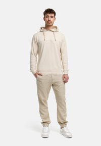 Beige hættetrøje med tekstureret stof, kontrasterende vandret panel og snor. Sammen med lysebeige joggerbukser og sneakers.