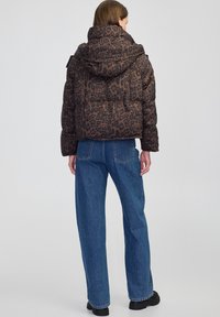 Bruine pufferjack met luipaardprint en capuchon, met een boxy silhouet. Gepaard met hoge taille blauwe spijkerbroeken en zwarte chunky laarzen.