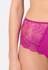 Slip in pizzo fucsia con motivo floreale, caratterizzato da un pannello superiore in pizzo trasparente e una sezione inferiore rosa solido. Dettagli con bordo scallop.