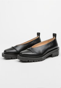 Scarpe in pelle nera con un design a taglio basso, caratterizzate da una striscia stretta nella parte anteriore e una suola in gomma spessa con battistrada.