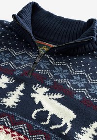 Pull en maille marine avec motifs d'inspiration nordique, élan blanc et pins, flocons de neige rouges et bleus, et col côtelé à fermeture éclair partielle.
