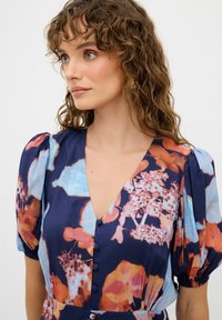 Blumengemustertes Kleid in Marineblau, mit Puffärmeln, einem V-Ausschnitt und Knöpfen entlang der Vorderseite. Helle Orange- und Blautöne.