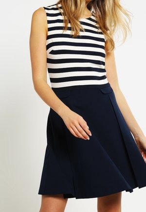 Donkerblauwe A-lijnrok met plooien aan de voorkant en twee zijzakken, gecombineerd met een mouwloze, wit-met-donkerblauw gestreepte top. Soepele stoftextuur.