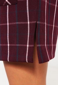 Falda de cuadros burdeos con rayas blancas y marino; presenta una abertura lateral y una tela texturizada, mostrando un diseño sin costuras.