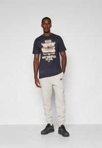 Marinblå t-shirt med grafik av en våffla och texten "HOT WAFFLES TO GO." Kombinerad med ljusgrå mjukisbyxor och svarta sportskor.